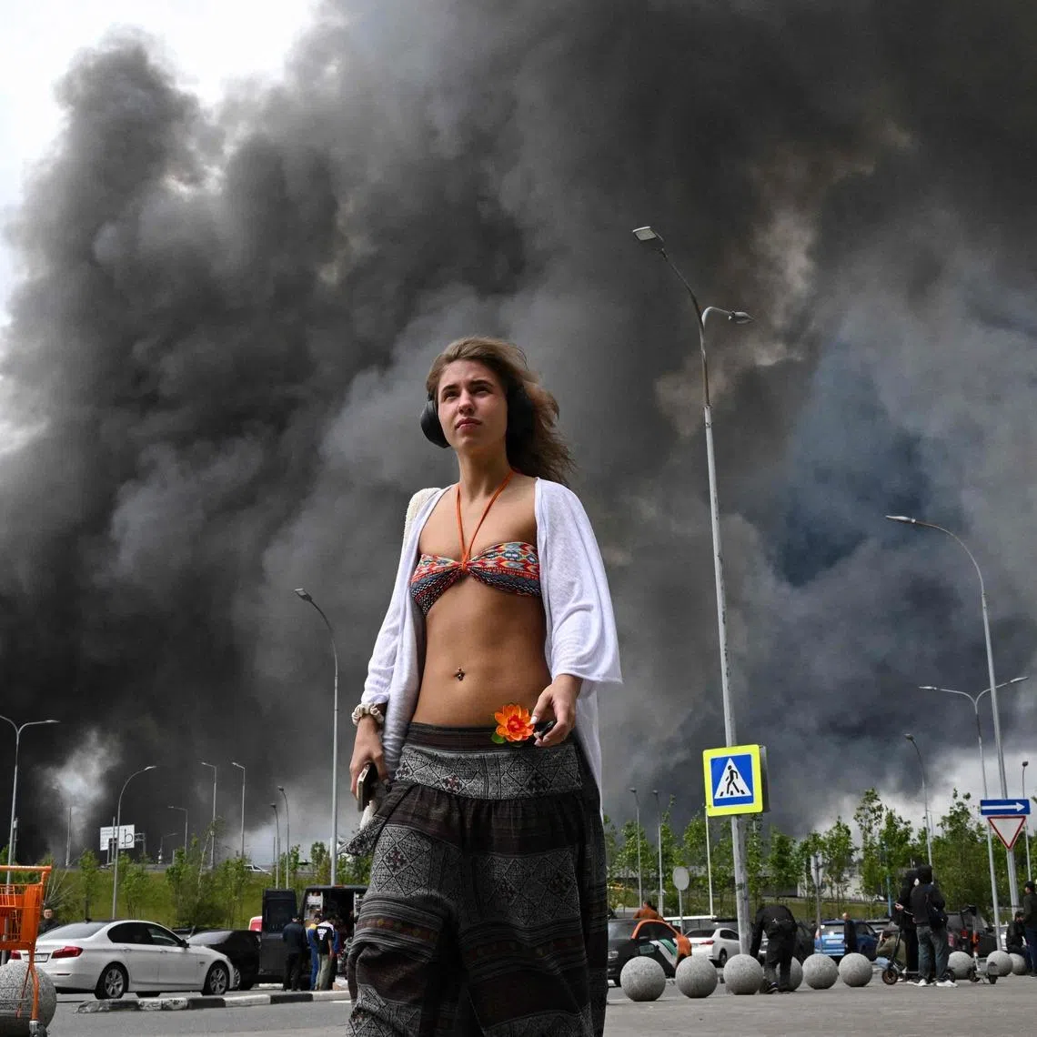 A woman walking past a shopping mall as black smoke rises from an oil refinery after a drone attack from Ukraine, on the south-eastern outskirts of Moscow on June 18, 2026. 
