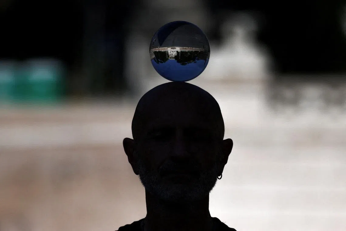 The reflection of Piazza del Popolo is seen in a crystal ball balanced on a performer’s head, in Rome, Italy, on May 27, 2026. 