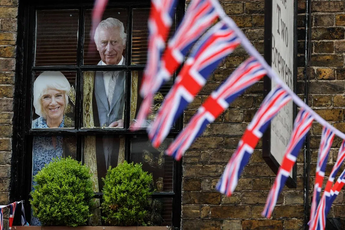 Cardboards picturing Britain's Camilla, Queen Consort (L) and Britain's King Charles III are displayed on the window of a pub in a street adorn with Union Jack flags, in Windsor, on May 2, 2023, ahead of the coronation ceremony of Charles III and his wife, Camilla.