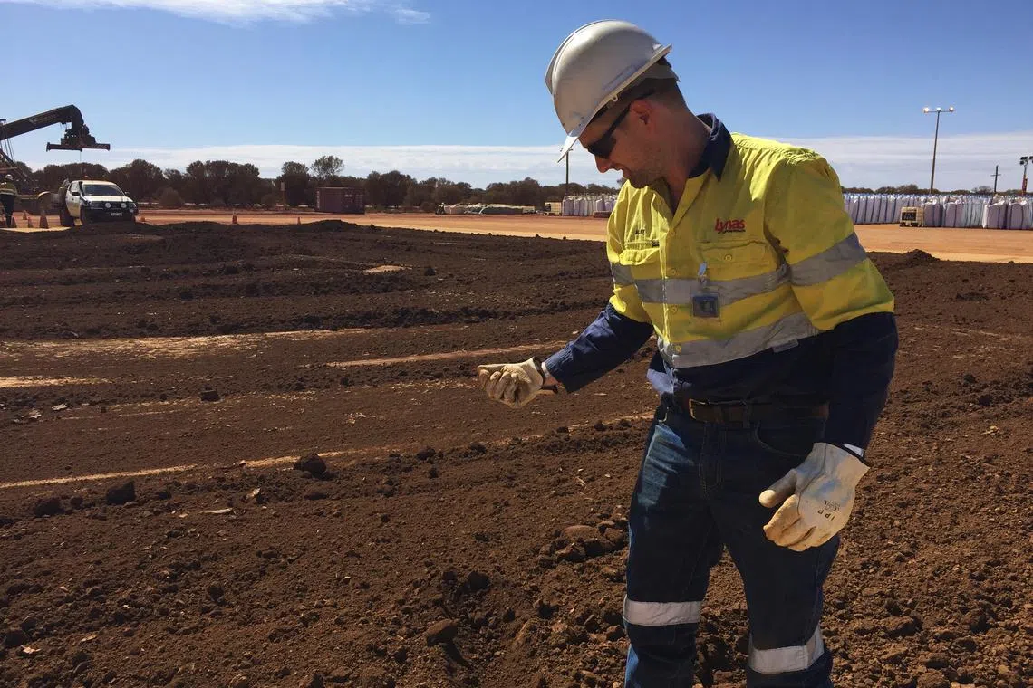 A worker picks up a handful of rare earth concentrate that has been left to dry in the sun at Mount Weld, northeast of Perth, Australia.