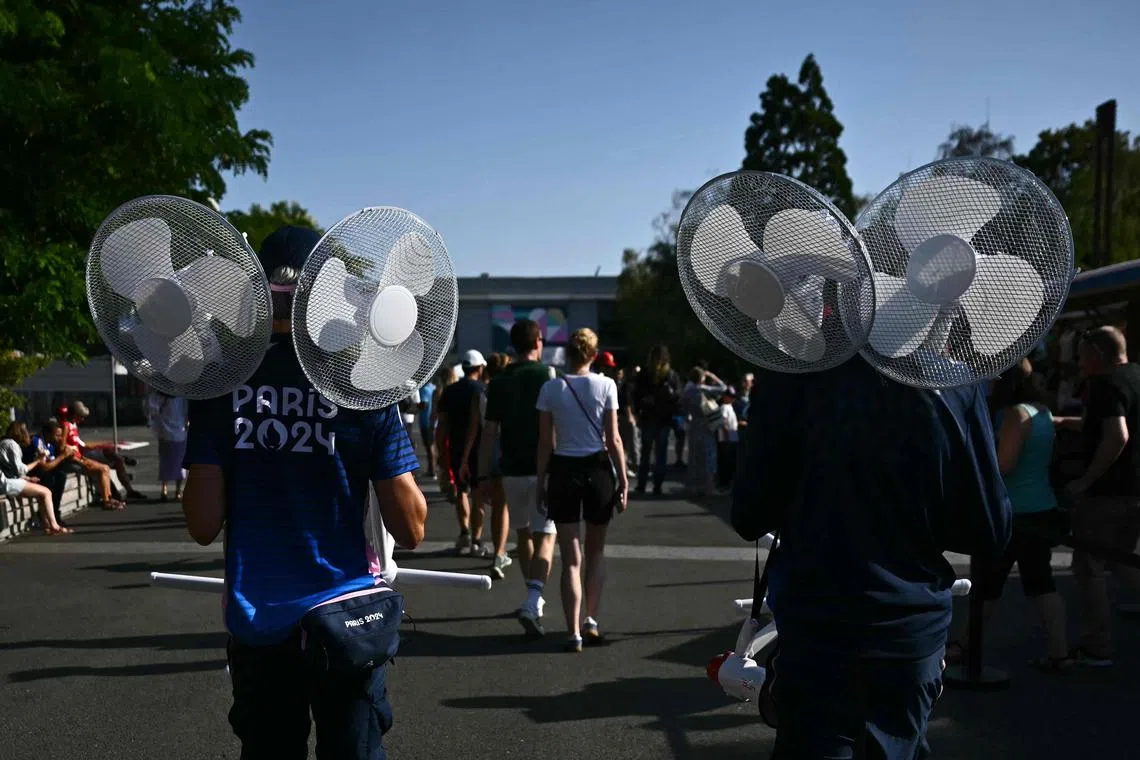Volunteers carry fans on a hot summer day during the Paris 2024 Olympic Games.