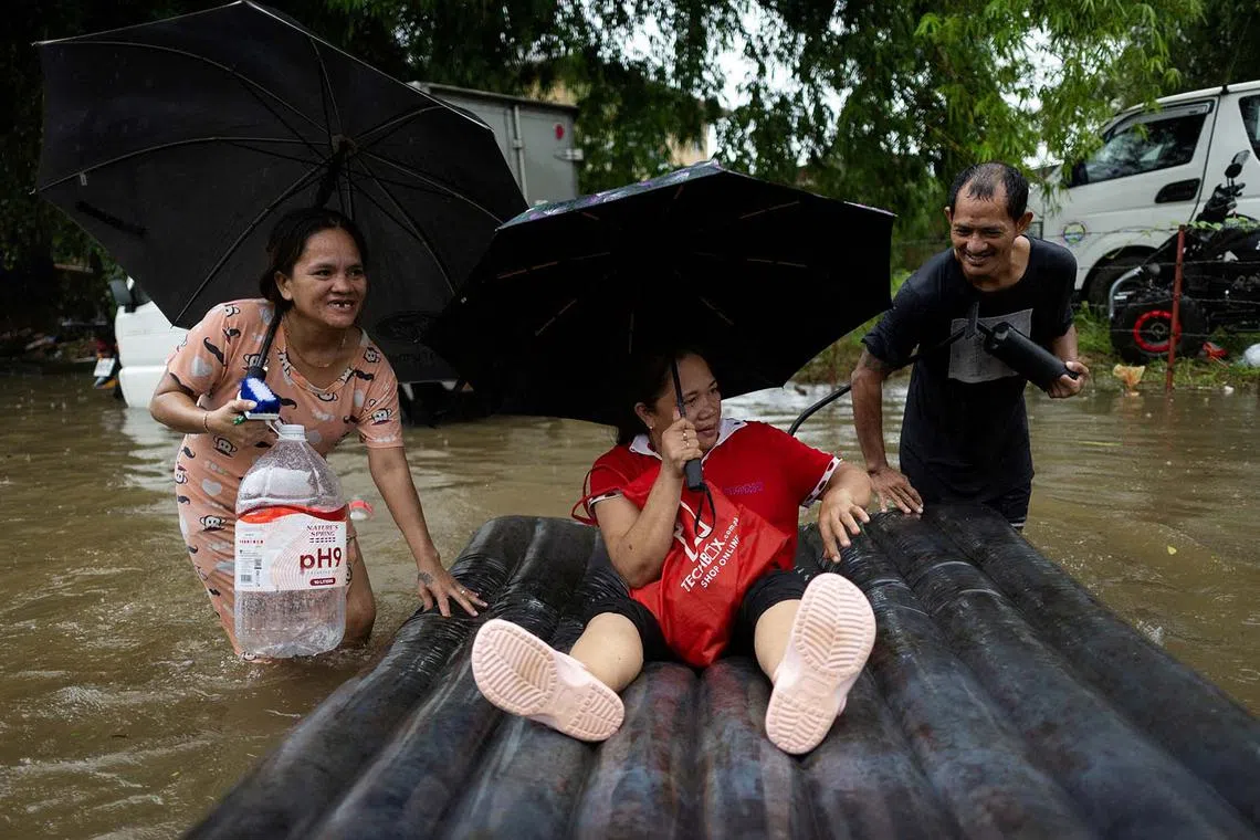 A woman floating on an inflatable bed as a couple pushes it through floodwaters following monsoon rains in Cainta, Rizal, Philippines, July 22, 2025. 