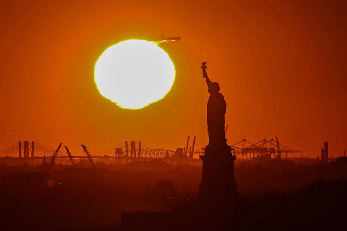 TOPSHOT - An airplane flies overhead as the sun sets behind the Statue of Liberty in New York on November 12, 2024. (Photo by ANGELA WEISS / AFP)