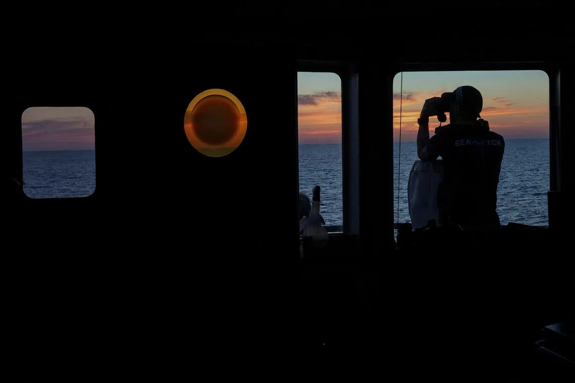 A crew member looking through binoculars, as the ship operates in the search and rescue (SAR) zone in the central Mediterranean, off Libya, on Aug 7, 2025. 
