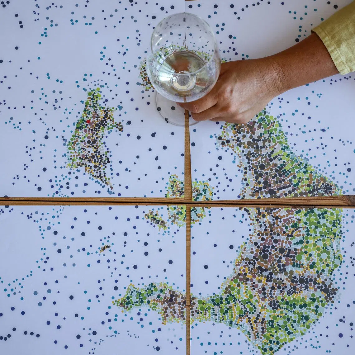 Ioanna Vamvakouri, president of the Santorini winemakers association holds a glass of awarded Assyrtiko wine at a placemat depicting the map of  Santorini island complex, in the winery at Therasia, Greece, June 24, 2026. REUTERS/Louisa Gouliamaki