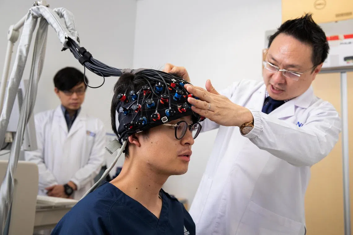 lxadhd26 - Professor Roger Ho (far right), 47, principal investigator at NUS iHealthtech, helping Mr Yudai Tanaka, 25, Year 6 medical student at Kanazawa University School of Medicine, to put on the infrared brain scan device, while Mr Chiang Soon Kiat (right), 27, biostatistician at NUS iHealthtech, sets the test up in the background at NUS iHealthtech on April 24, 2023.

File name: Infrared brain scan 1
Credit: Yong Li Xuan