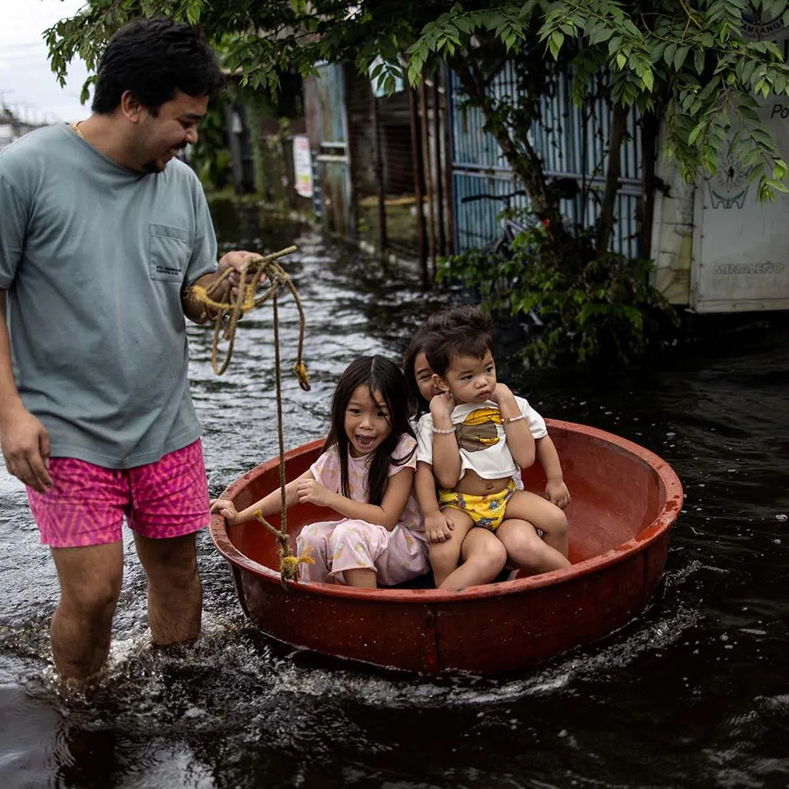 Children sitting in a basin reacting as they are pulled through a flooded area on Manila North Road following heavy rains brought by Typhoon Co-may in Minalin, Pampanga, Philippines, July 25, 2025. 