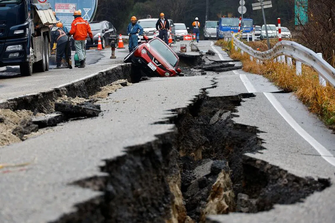 Workers repair a road next to a car stuck on a broken road, in the aftermath of an earthquake, near Anamizu, Japan, January 3, 2024. REUTERS/Kim Kyung-Hoon