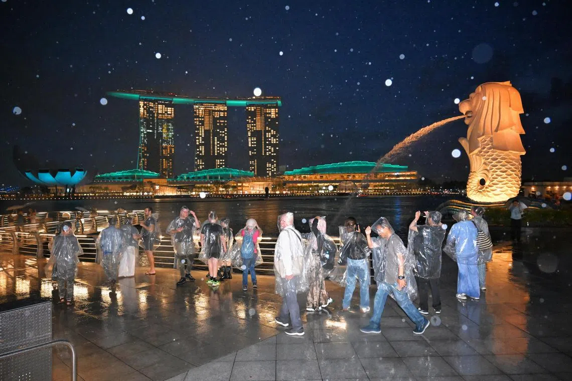 Tourists braving the rain against a the Marina Bay Sands which was lit up in green for the DrugFreeSG Light-Up 2024 on June 26, 2024. 
