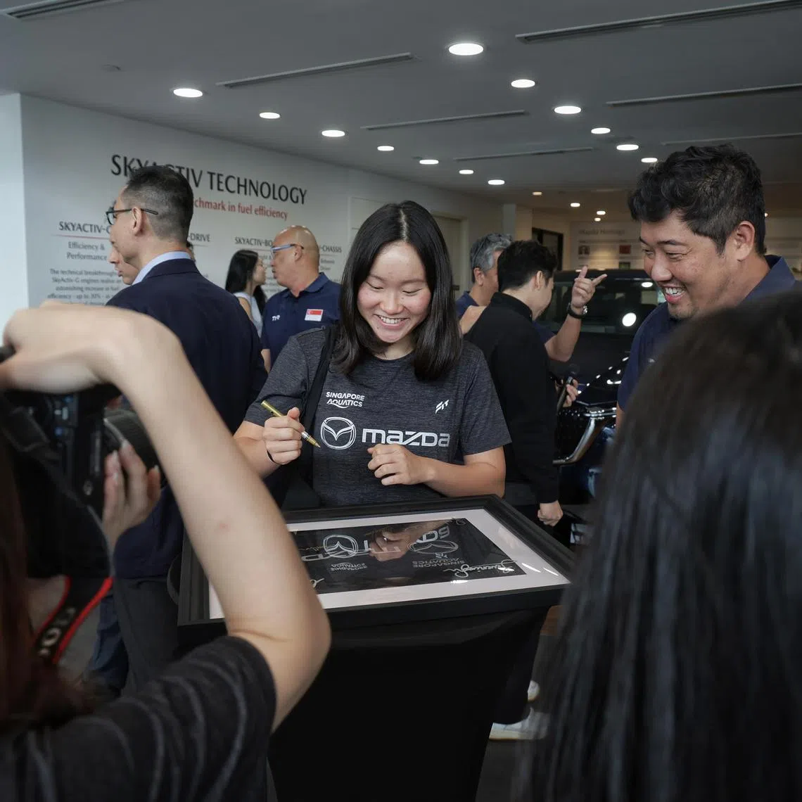 National swimmer Gan Ching Hwee signing an autograph on a framed t-shirt commemorating the sponsorship signing ceremony between Singapore Aquatics and Mazda Singapore on July 10, 2024. On the right is national swimming head coach Gary Tan. ST PHOTO: KEVIN LIM dgswim10
