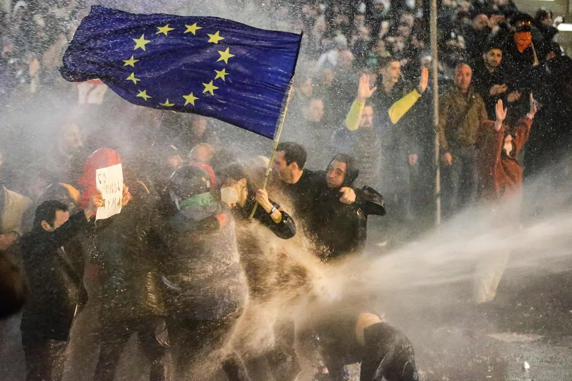 Protesters brandishing an EU flag are sprayed with a water cannon, during clashes with riot police near the Georgian parliament in Tbilisi, on March 7, 2023.