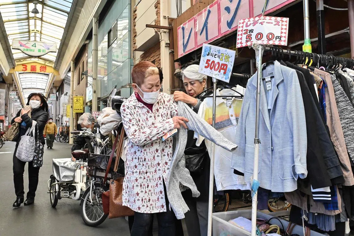 Shoppers trying on secondhand clothing for sale along a shopping street in Osaka. 
