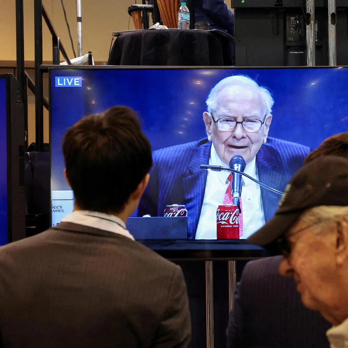 FILE PHOTO: People watch as Berkshire Hathaway chairman Warren Buffett is seen on a screen speaking at the Berkshire Hathaway Inc annual shareholders' meeting, in Omaha, Nebraska, U.S., May 3, 2025.  REUTERS/Brendan McDermid/File Photo