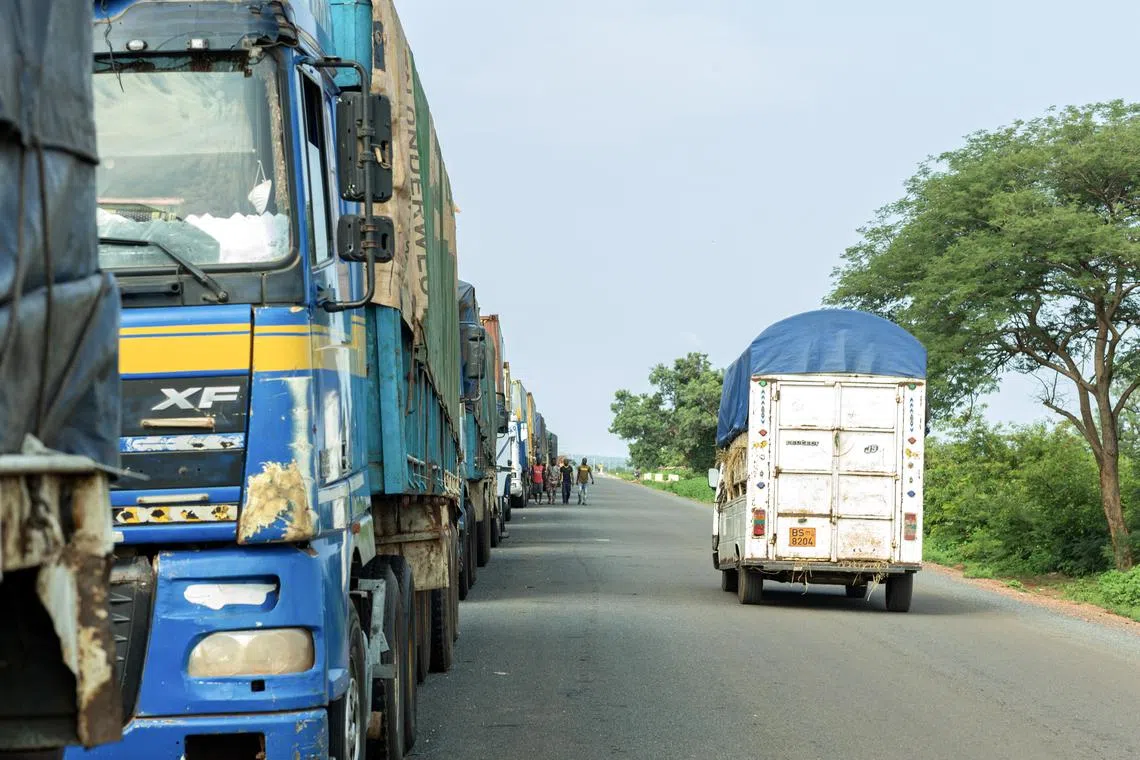 epa10802996 A vehicle drives past trucks parked on the side of the road near the border town of Malanville, Benin, 16 August 2023. Hundreds of trucks carrying produce and commercial goods have been stuck in the border town of Malanville following the closure of the border between Benin and Niger, amid sanctions imposed by the Economic Community of West African States (ECOWAS) following the coup in Niger.  EPA-EFE/DIDIER ASSOGBA