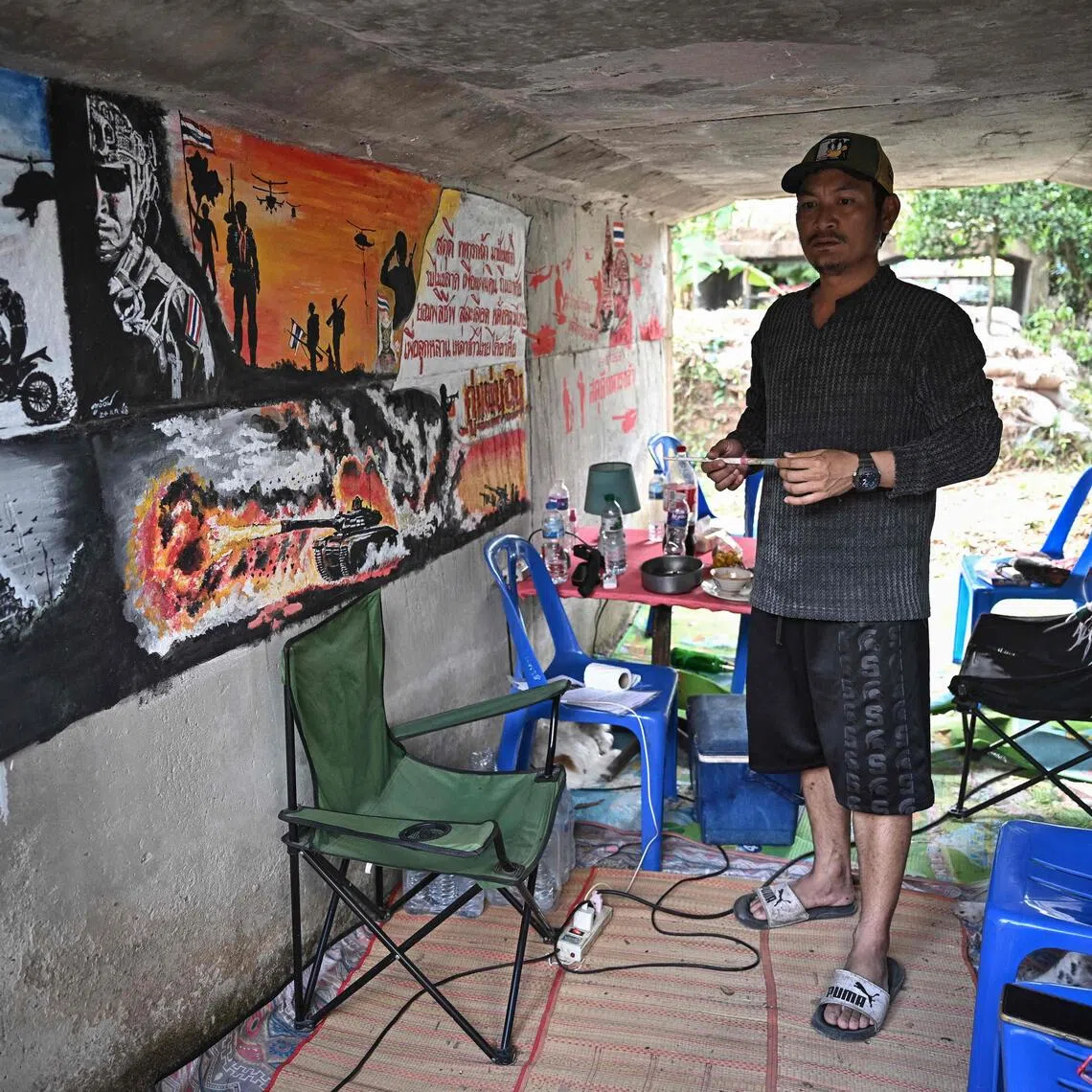 Thai teacher Watthanachai Kamngam with murals depicting the border conflict he painted in a bunker near his home in Surin.