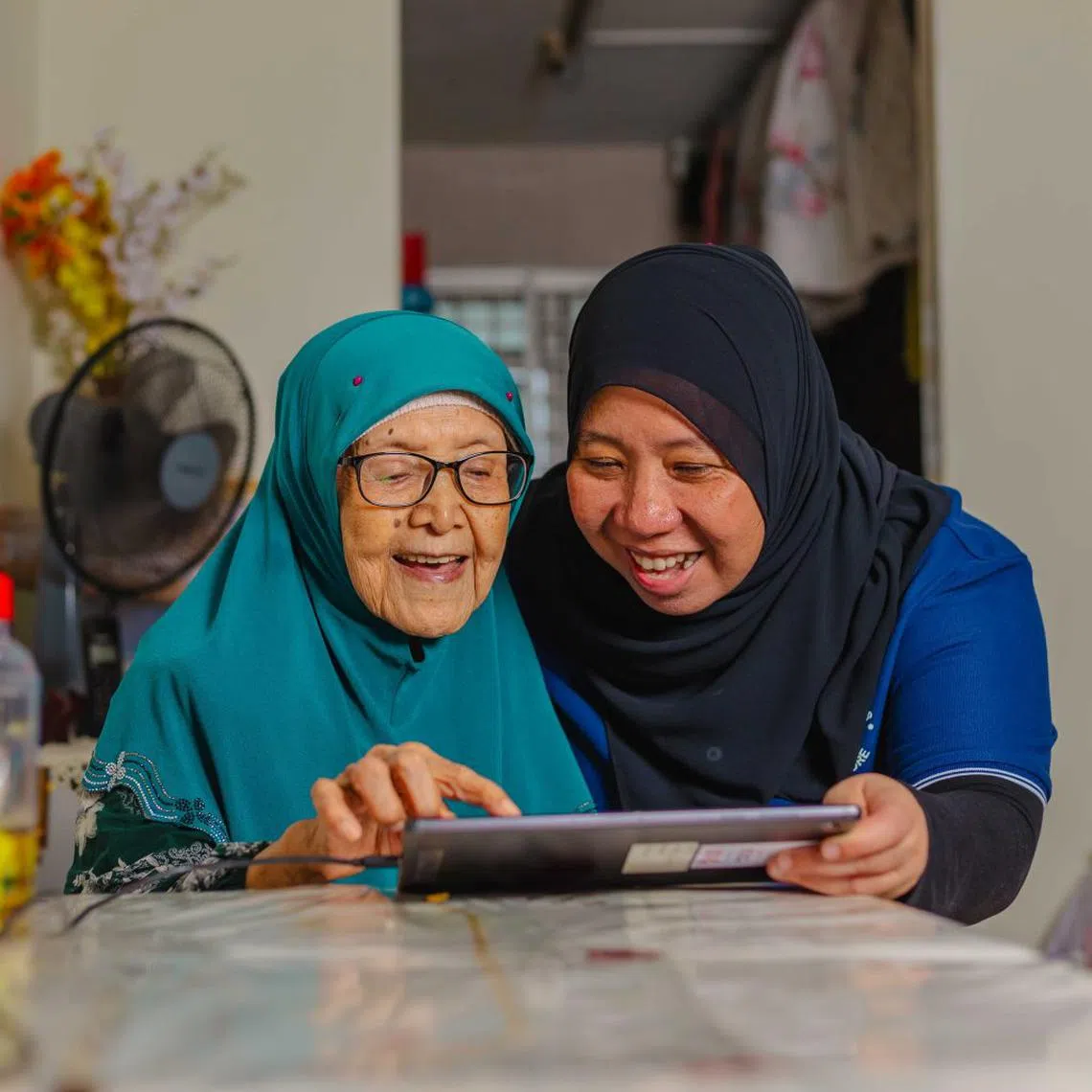 lions befrienders elder care staff zuraidah zainuddin teaching vulnerable senior zainab ahmad on how to use im ok tablet to well being remotely from home