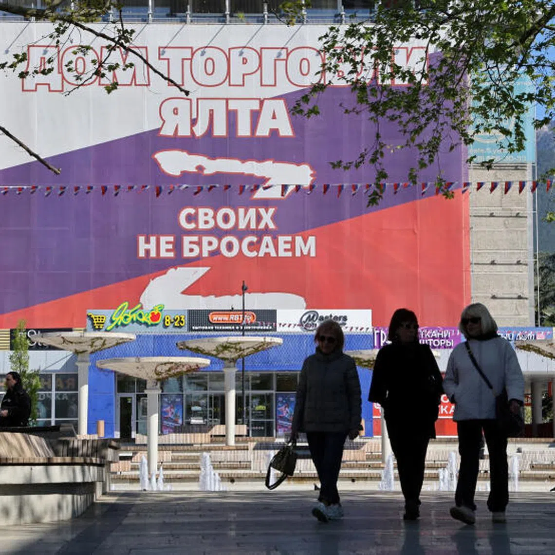 People walk along a street near a banner in the colours of the Russian flag reading "We don't abandon our people", in Yalta, Crimea April 27, 2025. REUTERS/Alexey Pavlishak
