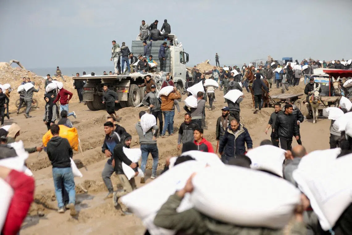 Palestinians carry bags of flour they grabbed from an aid truck near an Israeli checkpoint, on Feb 19.