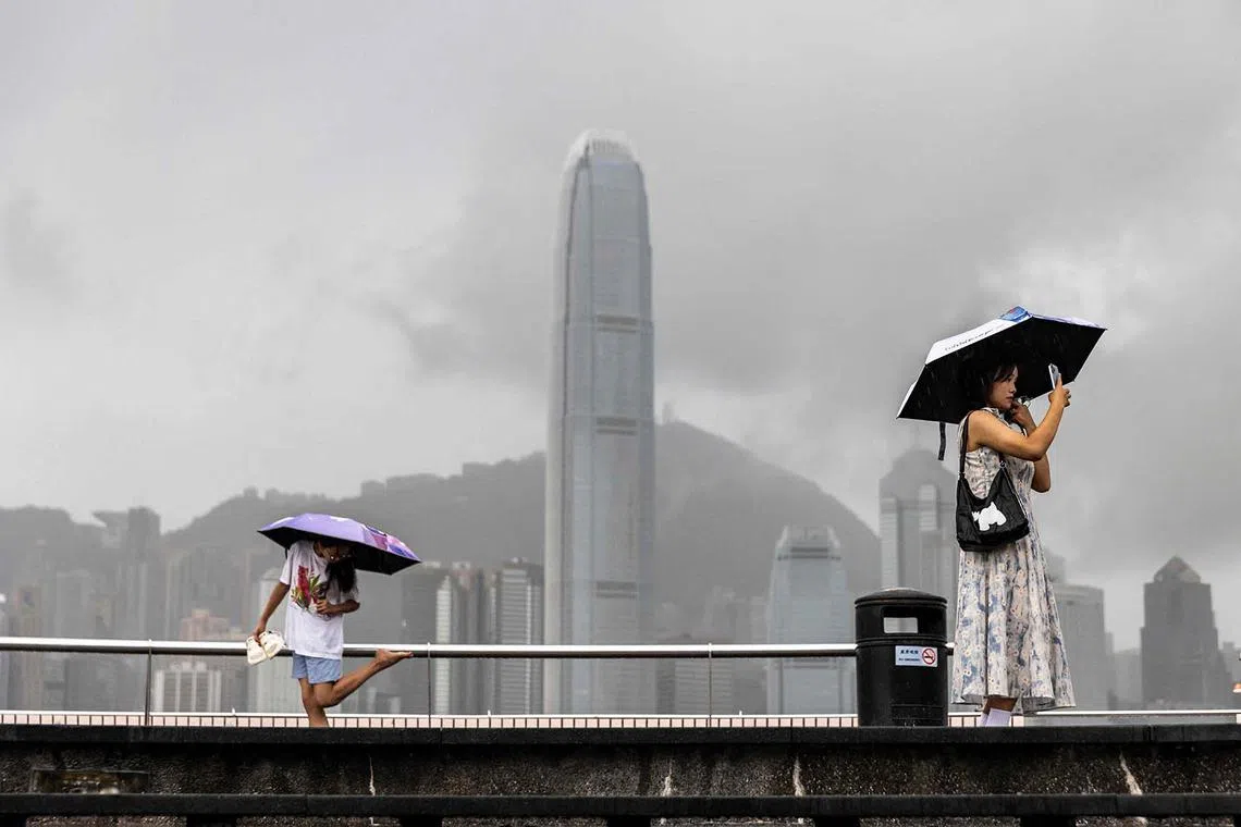 A woman (right) taking a photo next to Victoria Harbour in Hong Kong on Aug 14, 2025, as Typhoon Podul weakens to a severe tropical storm. 