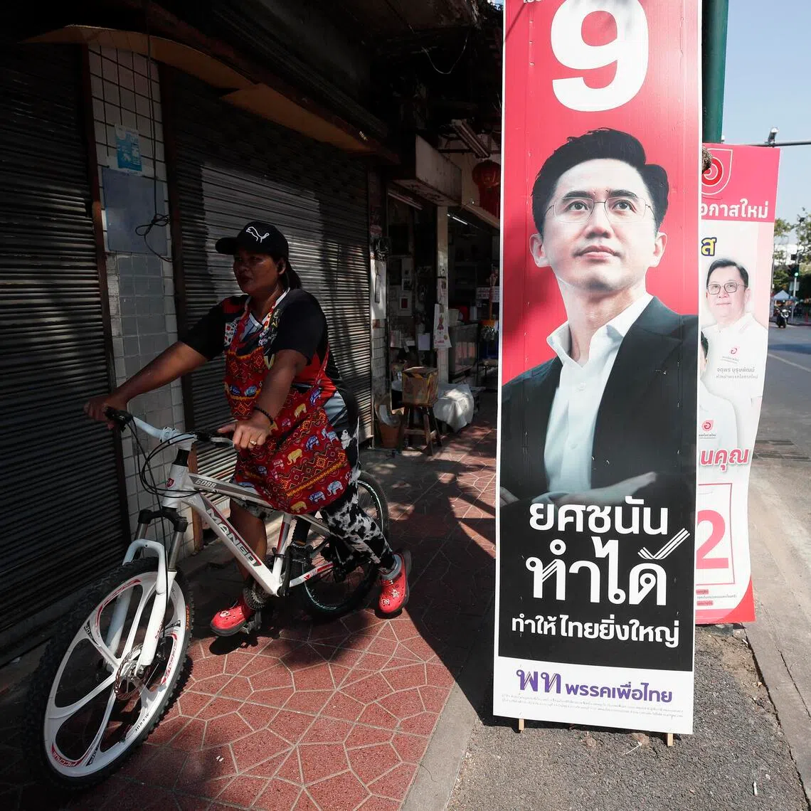 A Thai woman rides a bicycle past an election campaign poster of Pheu Thai Party's prime ministerial candidate Yodchanan Wongsawat.
