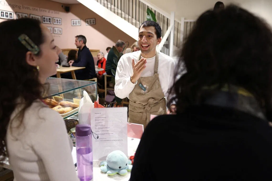 Zaki (centre) gets advice from skills coach Natalia, as they work in Fair Shot, a cafe set up to train young people with autism and other learning disabilities in employment skills, in central London, Britain, January 15, 2025.  REUTERS/Suzanne Plunkett