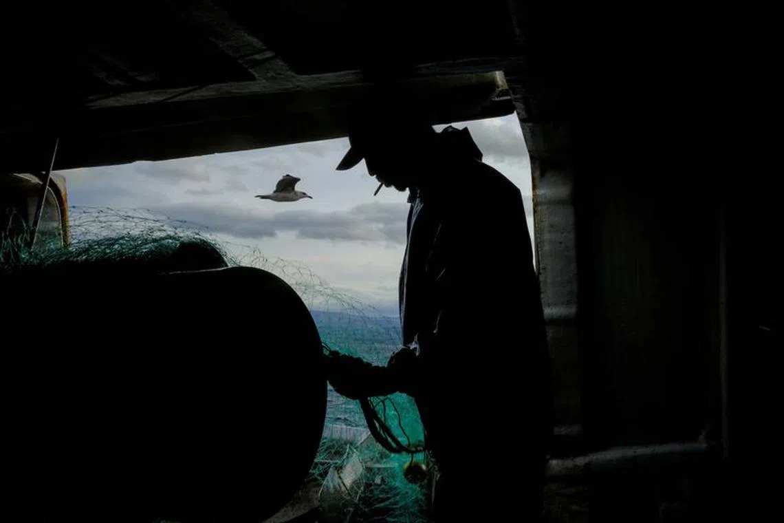 Babou Diouf, 46, a fisherman from Senegal, rolls up a fishing net on the Sarridal ship at the Cantabrian Sea, near Burela, Galicia, Spain, December 11, 2023. Diouf was part of a migration surge in 2006 from West Africa through Spain's Canary Islands, with more than 30,000 migrants fleeing poverty exacerbated by a dramatic plunge in coastal fish stocks. This record was broken in 2023 when nearly 7,000 people died. \"To see rafts arriving in Spain is very difficult,\" Diouf said. \"To cross the ocean without knowing what you're facing - you're facing death.\"      REUTERS/Nacho Doce