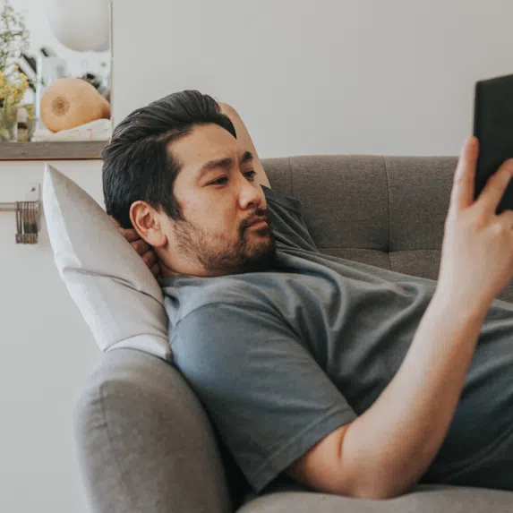 Kobo or Kindle: Chinese man lying down on a couch reading an e-reader
