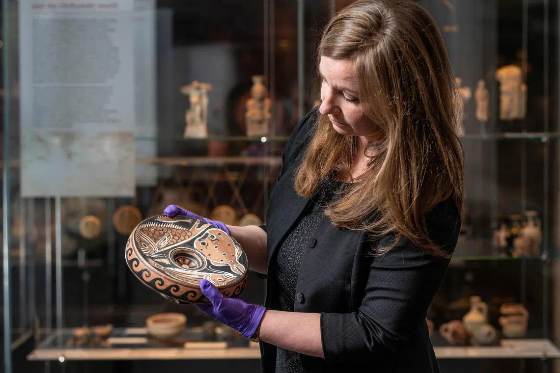 ANU Museum curator Georgia Pike-Rowney holding a red Apulian fish plate in Canberra.