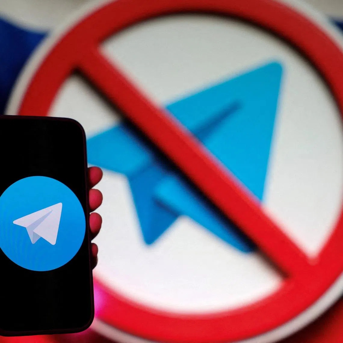 FILE PHOTO: A person poses for a photo while holding a smartphone next to a screen showing the crossed logo of Telegram messaging app against the backdrop of the Russian state flag, in this illustration taken February 12, 2026. REUTERS/Ramil Sitdikov/Illustration/File Photo