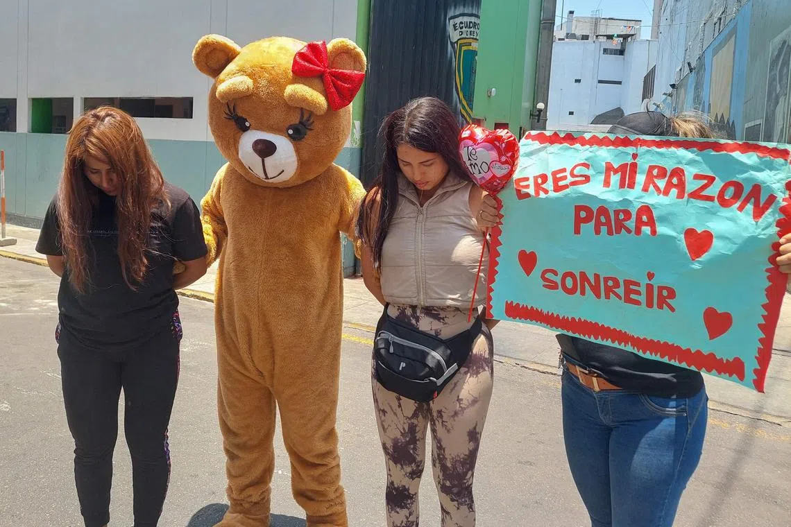 An undercover police squad member dressed as a giant Valentine's teddy bear poses with two alleged drug dealers after their arrest at a police station in Lima on Feb 14. 
