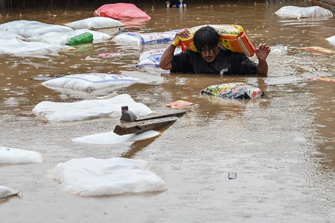 A man carrying a sack of flour wades through flood waters after the Bagmati River overflowed following heavy monsoon rains in Kathmandu on September 28, 2024. Floods and landslides caused by heavy downpours in Nepal killed at least 10 people across the Himalayan country, with rescue teams searching for 18 missing, a disaster official said on September 28. (Photo by PRAKASH MATHEMA / AFP)