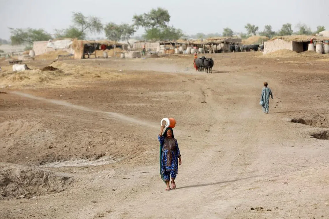 FILE PHOTO: A woman walks to fetch water from a nearby hand-pump with a water cooler on her head, during a heatwave, on the outskirts of Jacobabad, Pakistan, May 16, 2022. REUTERS/Akhtar Soomro/File Photo