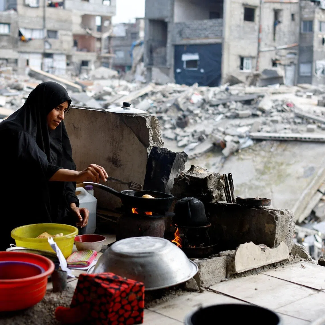 A Palestinian woman cooks amid the rubble of residential buildings destroyed during the war, in Jabalia, northern Gaza Strip, on Dec 31, 2025. 