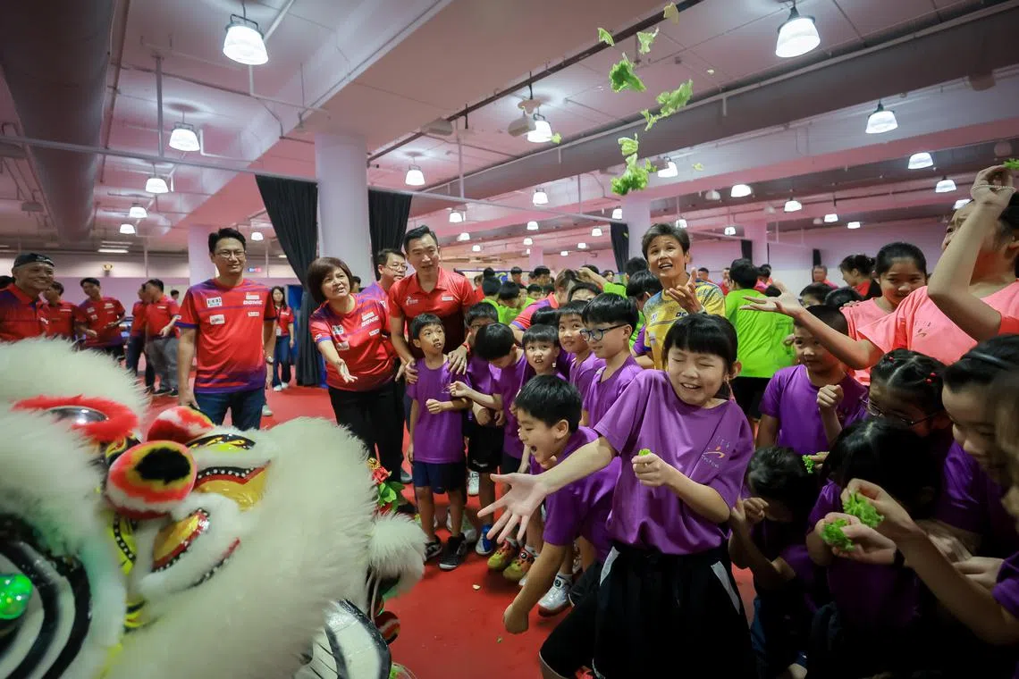 STTA President Poh Li San (back right, yellow top), Senior Parliamentary Secretary for the Ministry of Culture, Community and Youth, and the Ministry of Social and Family Development Eric Chua (3rd from left), STTA CEO Wong Hui Leng (2nd from left), Organising Chairman of STTA Opening Ceremony Subcommittee Toh Ern Chong (left) and children from STTA Kallang Zone Training Centre catching lettuce thrown by the lion dancers at the Singapore Table Tennis Association’s new headquarters grand opening at OCBC Arena, Nov 17, 2023.