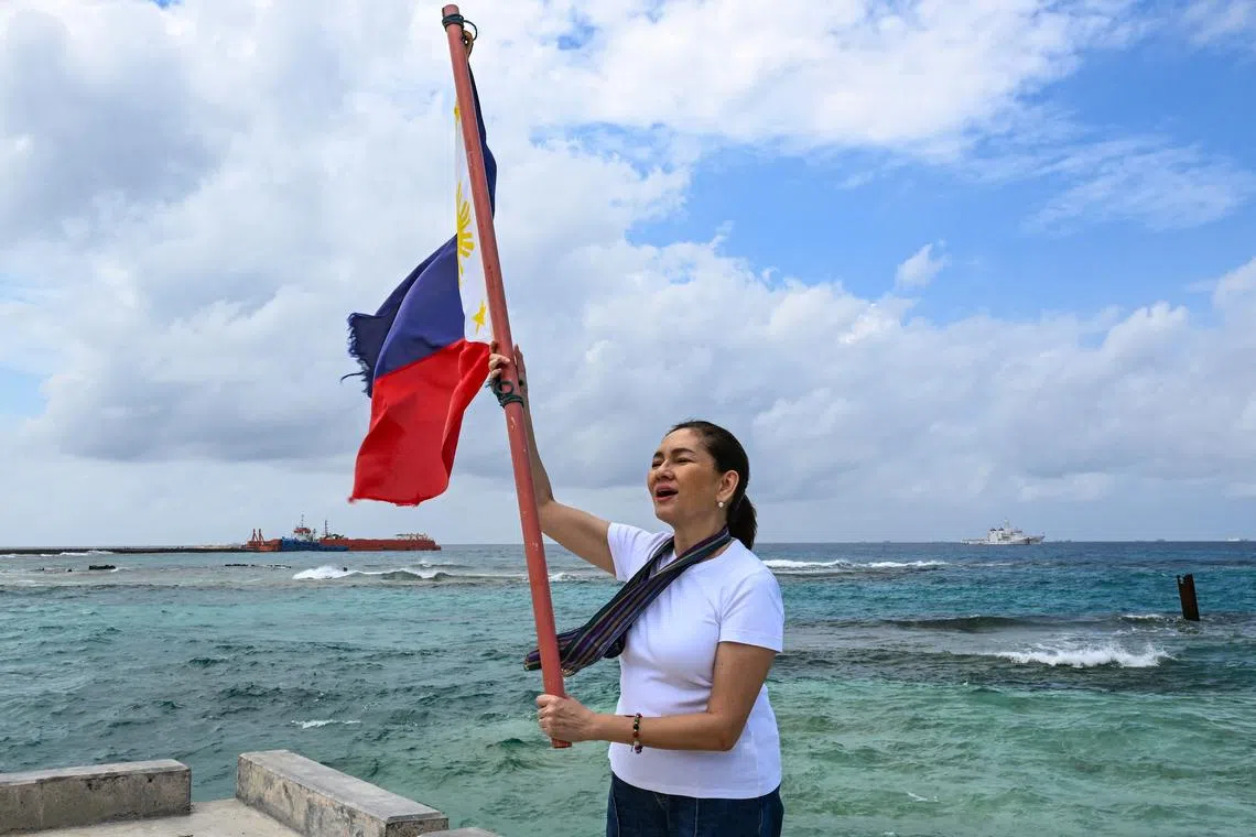 Philippine Senator Risa Hontiveros raises a Philippine flag on Thitu Island in the South China Sea on February 21, 2026. A Philippine senator called for deepening defence relationships and "continuous" pushback against China's claims in the South China Sea while visiting one of Manila's tiny possessions in the disputed waterway on February 21. (Photo by Jam STA ROSA / AFP)