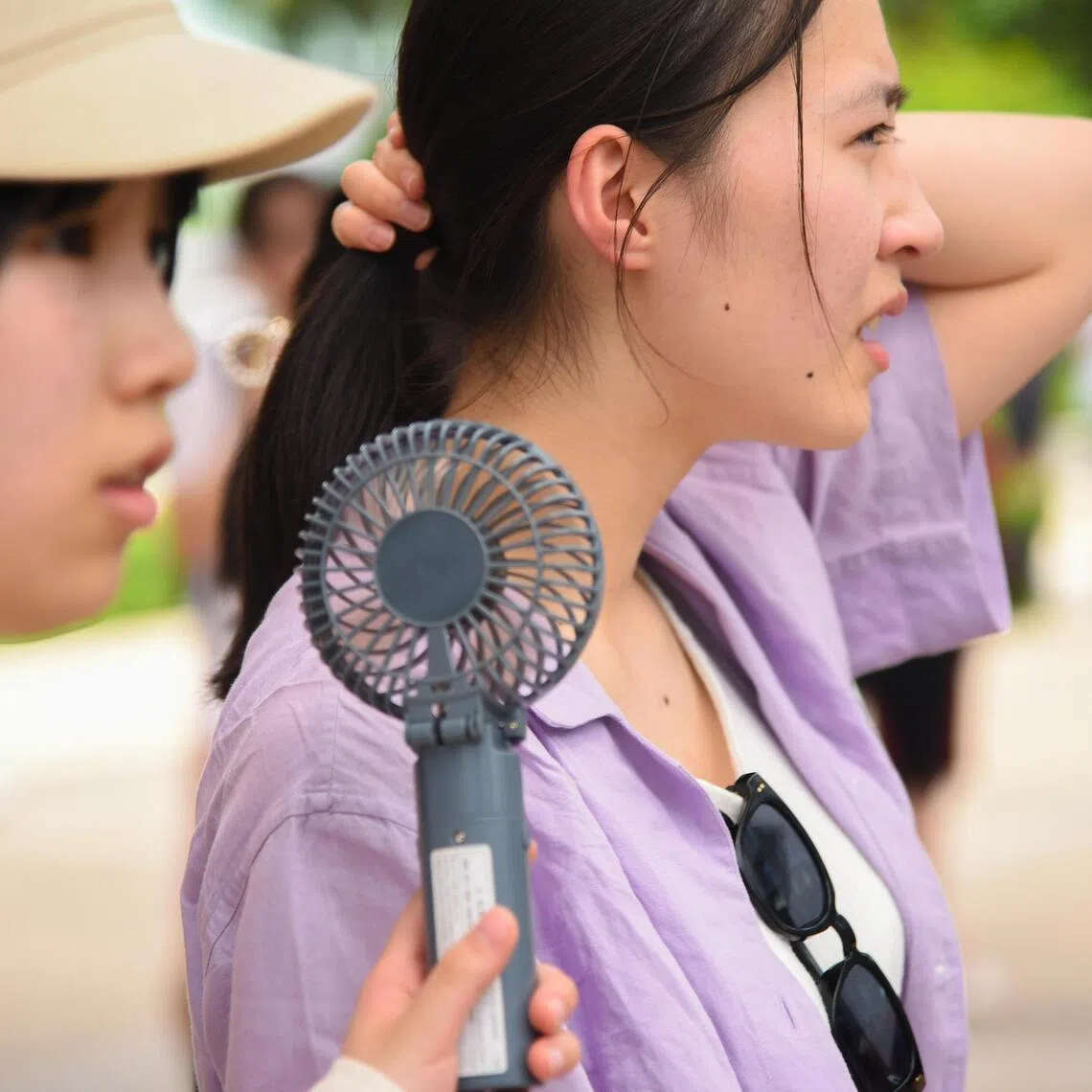 A woman holding her hair up while her friend points a handheld fan towards her at Universal Studios Singapore.