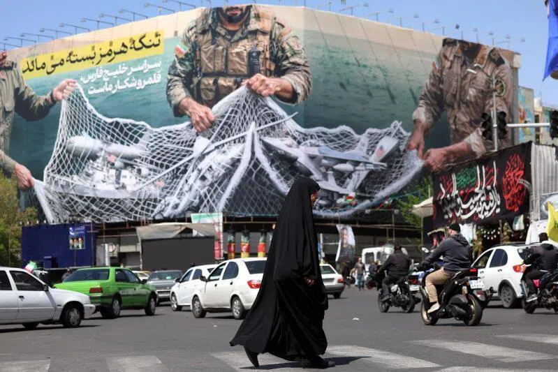 Commuters make their way past a billboard with a sentence reading ‘The Strait of Hormuz remains closed’ at the Enqelab Square in Tehran, on April 5, 2026. Oman and Iran held talks on easing passage through the Strait of Hormuz, the Omani state news agency reported on April 5, with the key shipping chokepoint effectively closed due to war in the Middle East. 