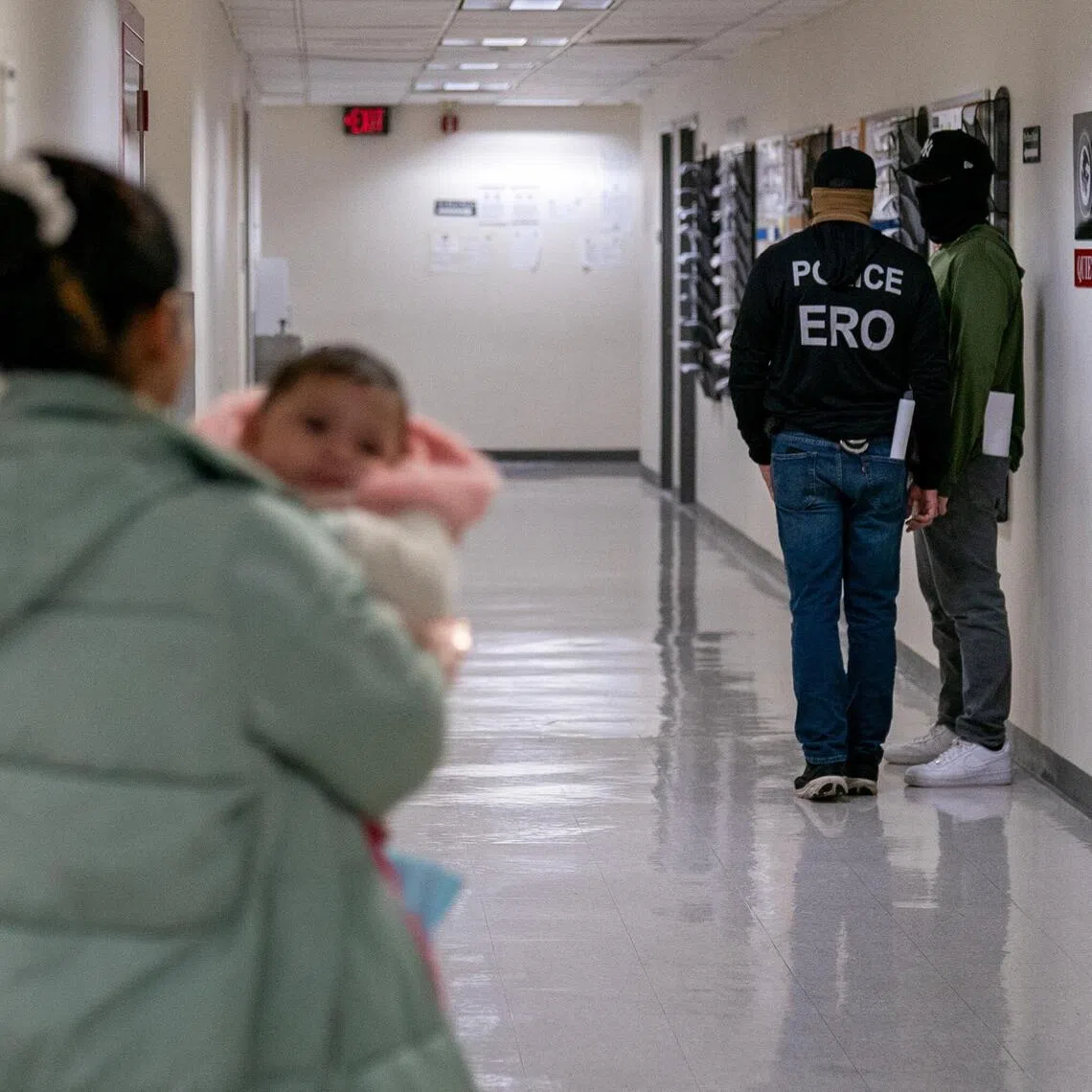 A woman carrying a child walks toward Immigration and Customs Enforcement (ICE) agents in the hallway of the U.S. immigration court in Manhattan, New York City, on Dec 18, 2025