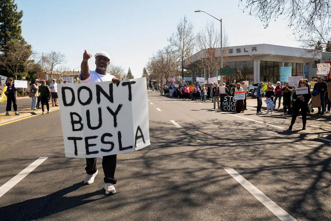 People protest against Tesla and Elon Musk outside of a Tesla dealership in Palo Alto, California, U.S on M