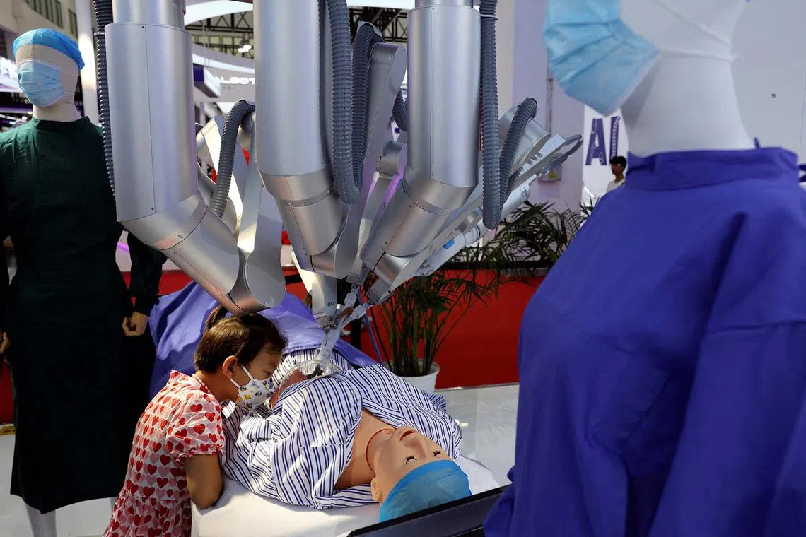 A child watches as a Shurui surgical robot, operated by a staff member (not pictured) from a console, performs "surgery" on a dummy at the World Robot Conference in Beijing, China, Aug 21, 2024. 