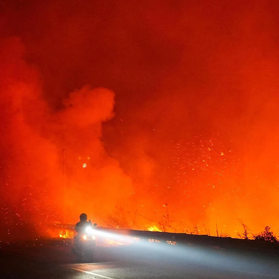 A motorist rides through a road as a wildfire burns near the main road in Ogan Ilir, South Sumatra province, Indonesia, September 11, 2026. REUTERS/Abriansyah Liberto     TPX IMAGES OF THE DAY