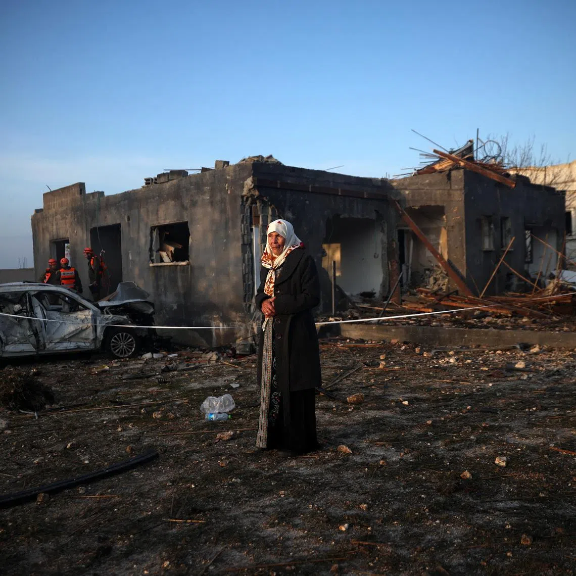 A woman stands as Israeli emergency responders work at the site of an impact by an Iranian missile, amid the U.S.-Israel conflict with Iran, in northern Israel, March 13, 2026. REUTERS/Shir Torem