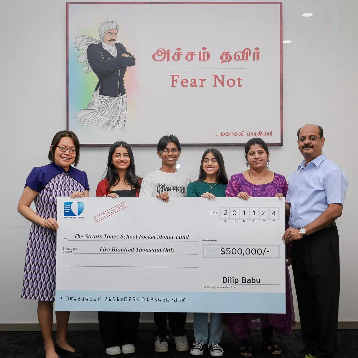 Ms Lee Su Shyan (left), fund trustee and The Business Times associate editor (news), receiving a donation of $500,000 for The Straits Times School Pocket Money Fund from Mr Dilip Babu, CEO of Info-Tech Systems Integrators and JobsLah.com on Nov 20, 2024. With him are (from 2nd right) his wife Ramya, 44, and their children Harini, 16, Arjun, 15, and Srinithi, 20.