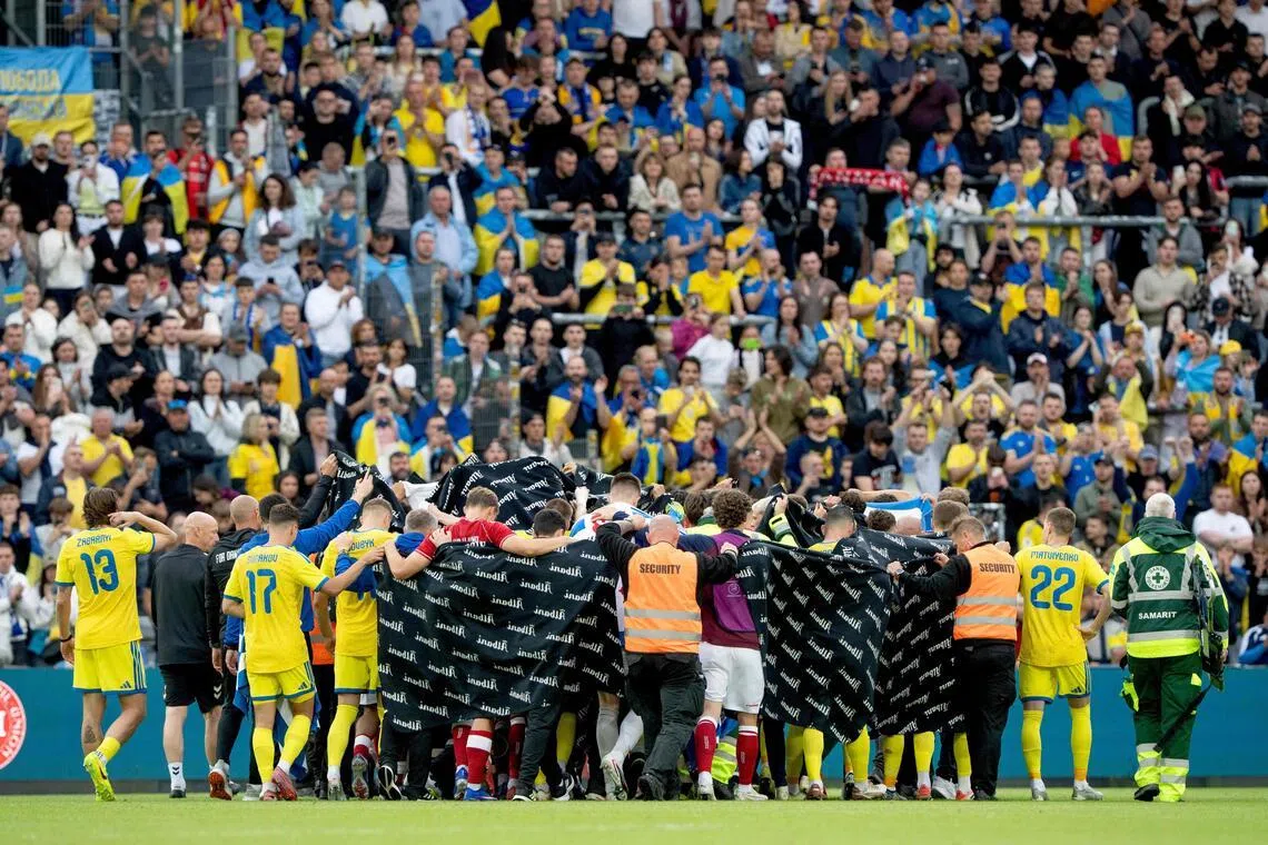 Denmark and Ukraine's players huddling to accompany Denmark's midfielder Christian Eriksen to a waiting ambulance during the international football friendly match between Denmark and Ukraine at Odense Stadium in Denmark, on June 7, 2026.