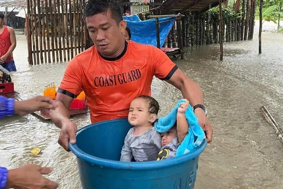 A member of the Philippine Coast Guard carries children affected by floods on a basin during a rescue operation, in Zamboanga City, Zamboanga province, Philippines, January 11, 2023. 