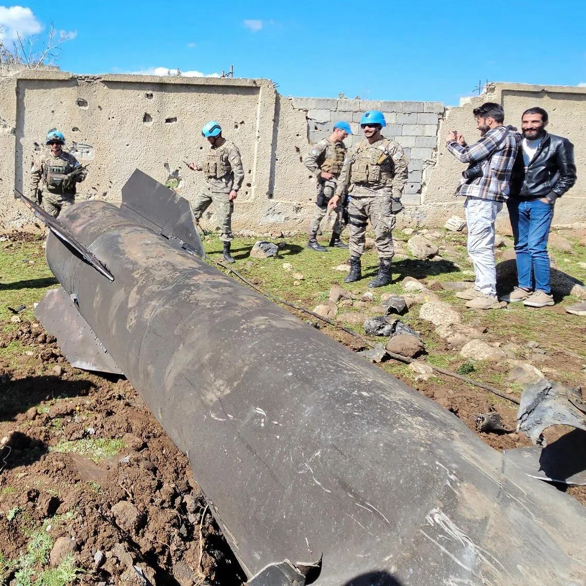 United Nations peacekeepers and civilians standing near the wreckage of an Iranian rocket that was reportedly intercepted by Israeli forces, in the southern Syrian countryside of Quneitra, near the Golan Heights, close to the town of Ghadir al-Bustan. 