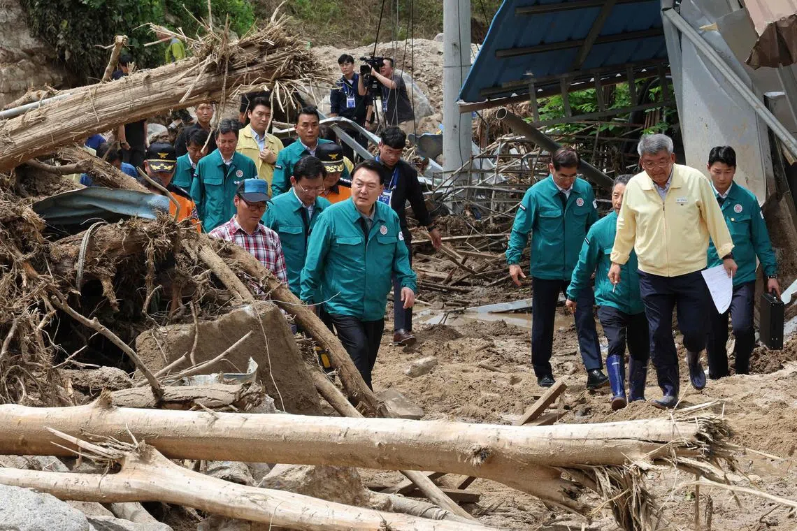Mr Yoon (centre) walks past piles of fallen trees at a village, where more than a third of houses were damaged in landslides.