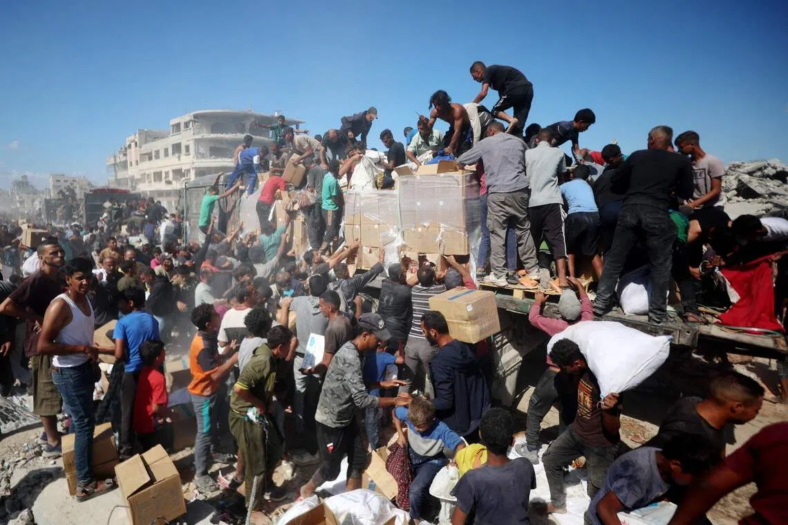 Palestinians collecting aid parcels from aid trucks which entered from the Karem Abu Salem crossing, in Khan Yunis in the southern Gaza Strip on Oct 12, 2025, as a ceasefire between Israel and Palestinian factions holds in the besieged territory. 