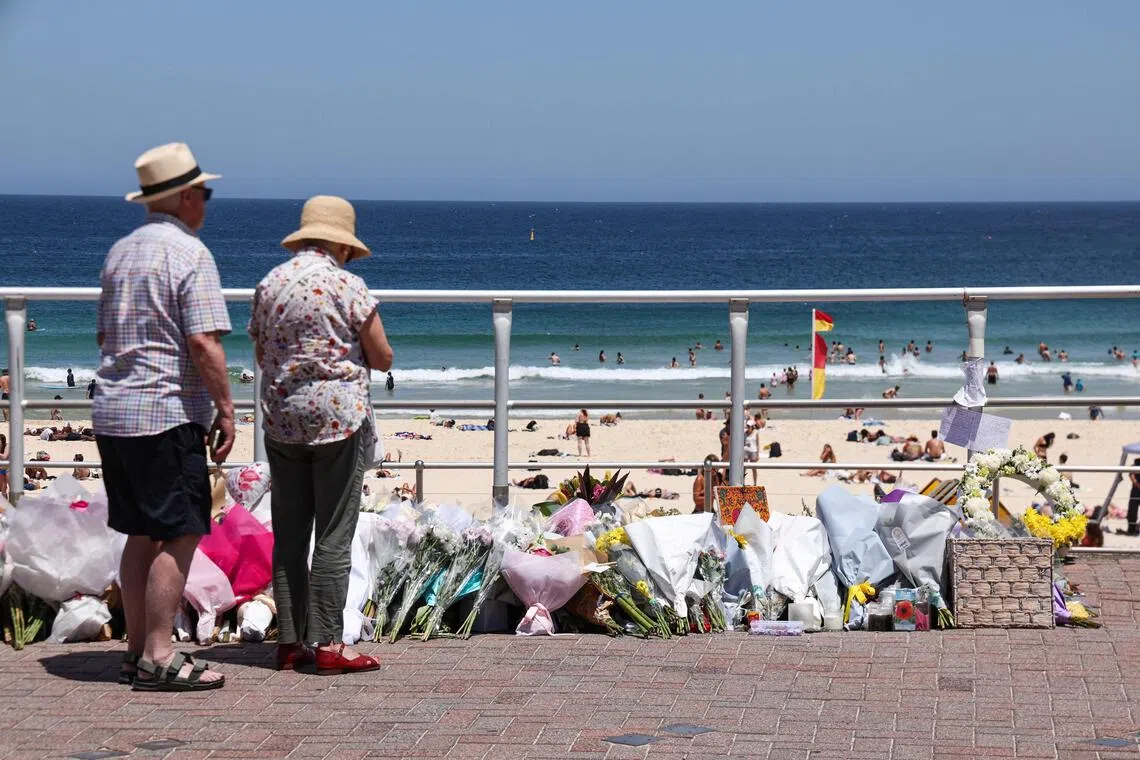 People stand in front floral tributes left at the promenade of Bondi Beach in Sydney on December 18, 2025, to honour victims of the shooting that took place there on December 14. The attack at Bondi Beach on December 14 was one of the deadliest in Australian history. (Photo by DAVID GRAY / AFP)