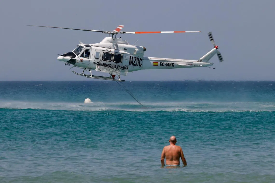 A helicopter draws water at Atlanterra beach as it battles wildfires in Tarifa, Spain.